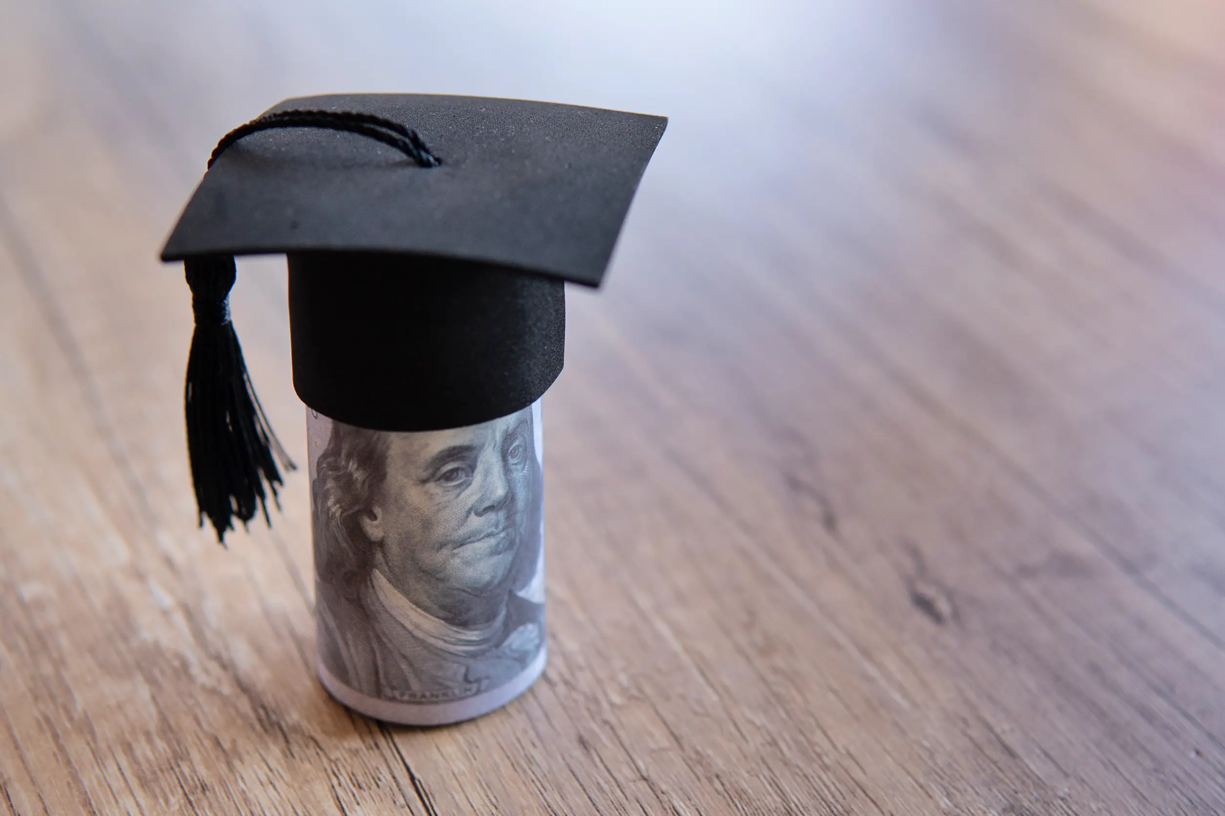 coiled $100 dollar bill with graduation cap